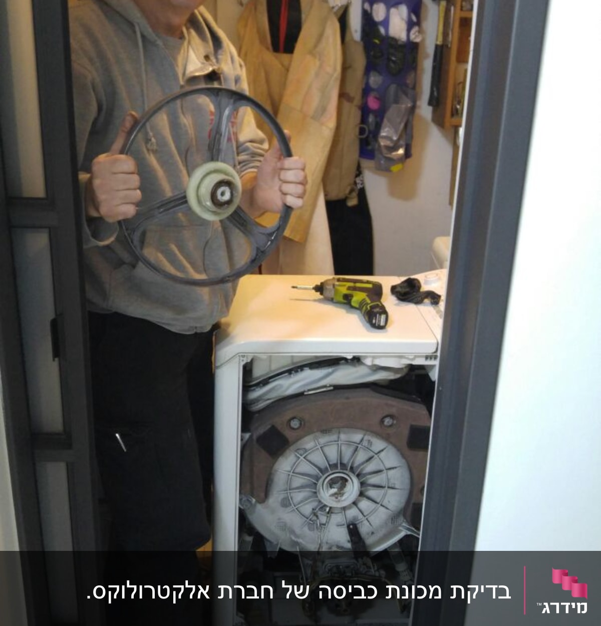אדם מחזיק גלגל מכונת כביסה, מברגה על המכונה
